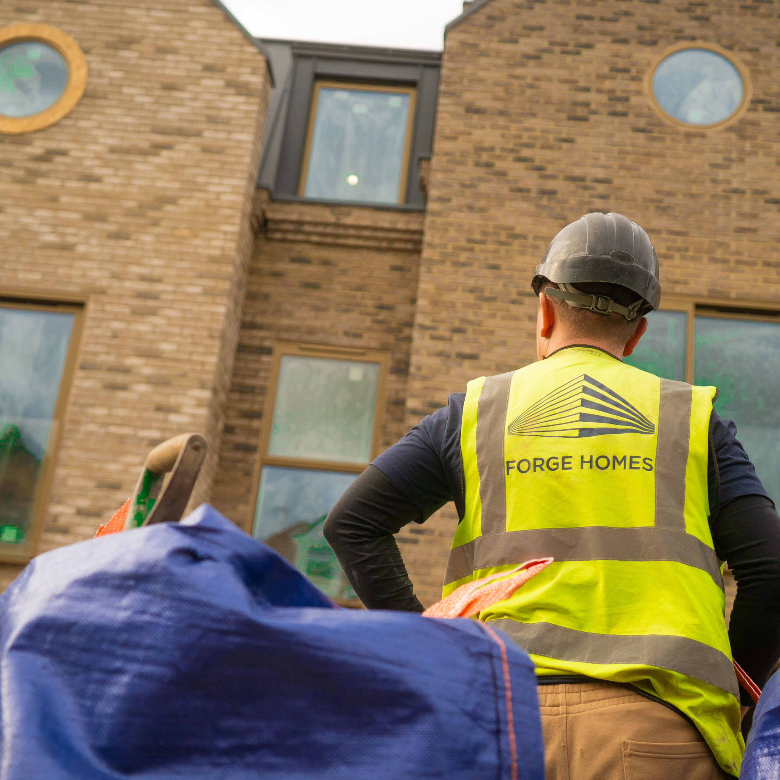 A construction worker looking at a new development. Wearing Hi Vis and Helmet with Forge Homes branding. PPE is always worn as health and safety is very important on site
