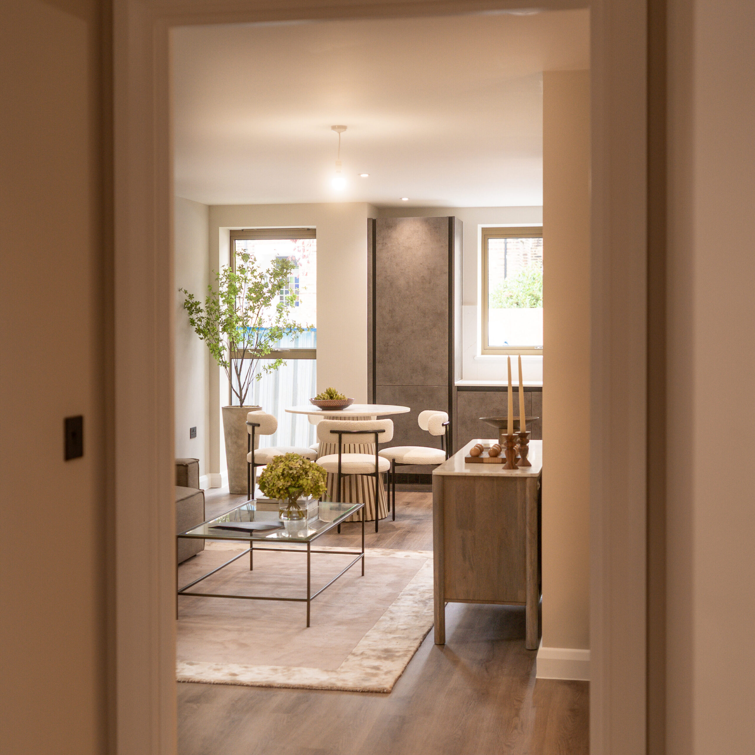 Shot from the hallway of the open plan living and kitchen area. Dark brown flooring and both the glass coffee table and dining room table