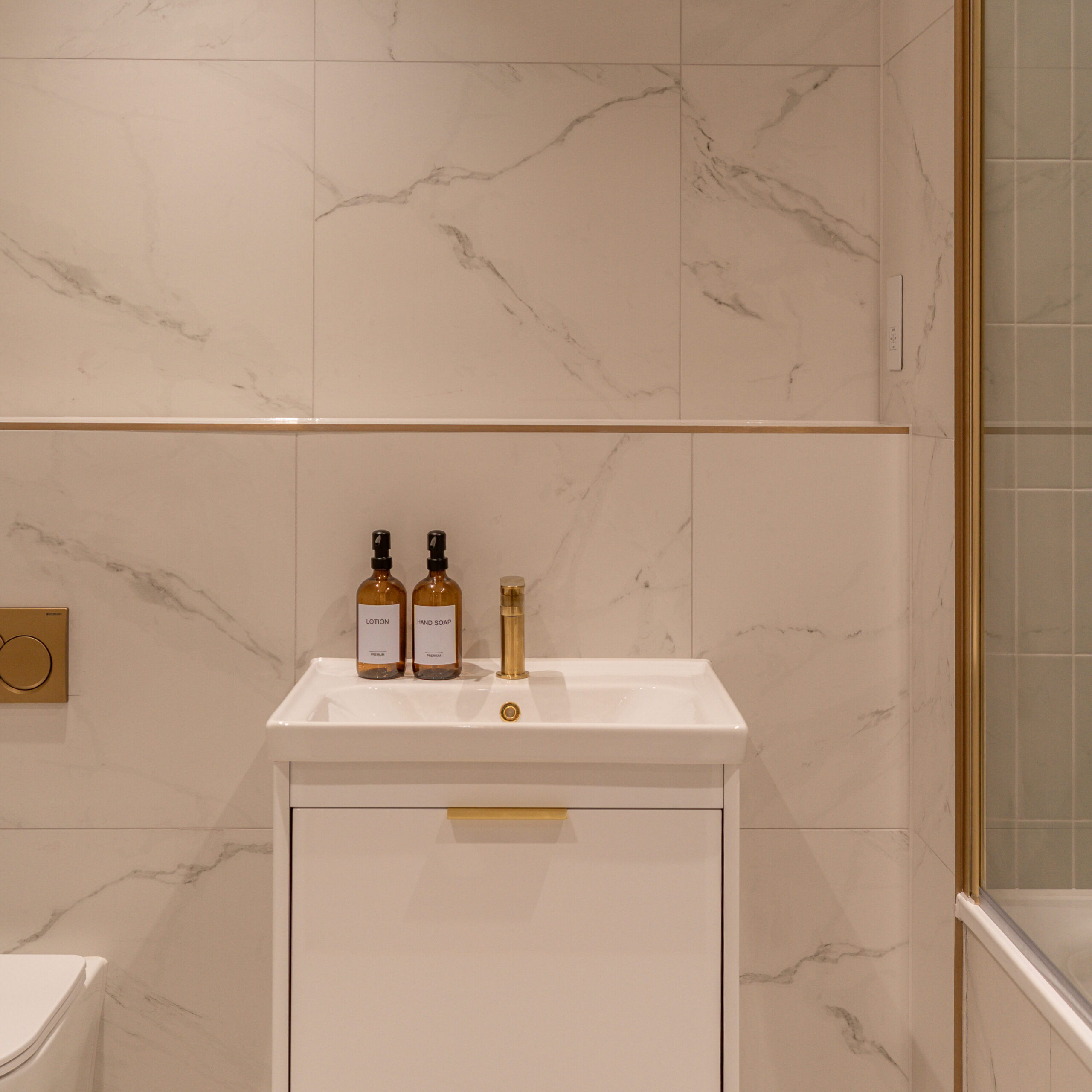 Shot of the main bathroom with the floating white sink basin with gold features. White marble tiling and gold features.