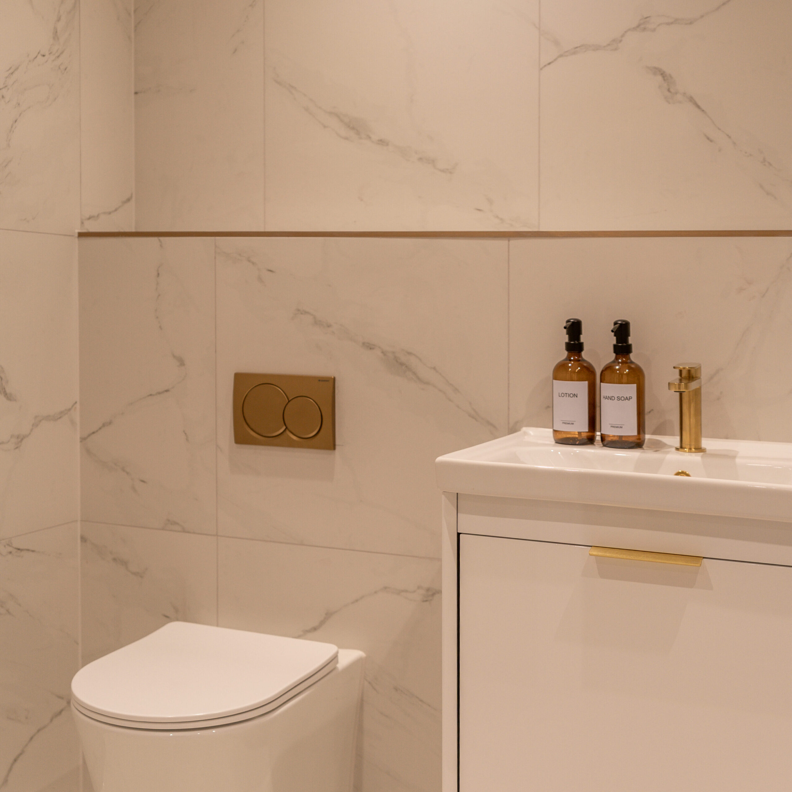 Shot of the main bathroom with the floating white sink basin with gold features. White marble tiling and gold features. White toilet